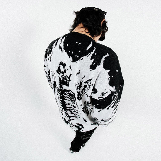 A man in a black and white skull shirt, striking a cool pose with a confident expression.